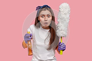 Home cleaning concept. Surprised terrified young woman from cleaning service, carries white brush to remove dust