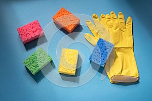 Home cleaning supplies: sponges and yellow rubber gloves on blu background