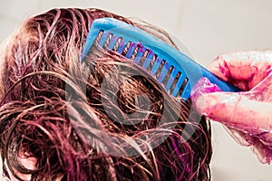 Home coloring of blonde hair: pink paint is applied to the head, hands in gloves hold a hairbrush