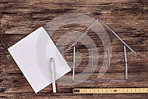 Home concept. Wooden model house on a work table with tools and empty spiral notebook