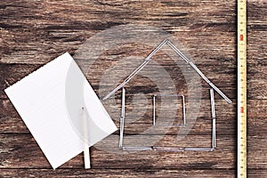 Home concept. Wooden model house on a work table with tools and empty spiral notebook