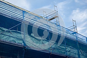 Home construction.Construction and repair of the house.Scaffolding in a protective blue grid against a cloudy sky