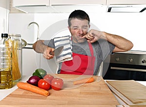 Home cook man in red apron slicing carrot with kitchen knife suffering domestic accident cutting hurting finger