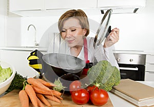 Home cook woman in red apron at domestic kitchen holding cooking pot with hot soup smelling vegetable stew photo