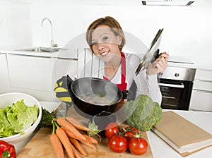 Home cook woman in red apron at domestic kitchen holding cooking pot with hot soup smelling vegetable stew