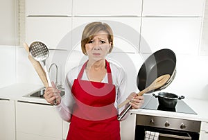 Home cook woman in red apron at domestic kitchen holding pan and household in stress