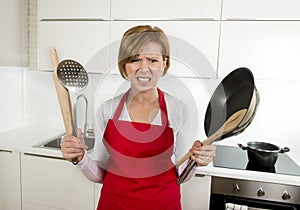 Home cook woman in red apron at domestic kitchen holding pan and household in stress