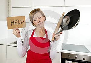 Home cook woman in red apron at domestic kitchen holding pan and household in stress