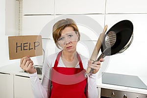 Home cook woman in red apron at domestic kitchen holding pan and household in stress