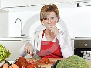 Home cook woman in red apron slicing carrot with kitchen knife suffering domestic accident cutting hurting finger