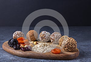 Home-cooked energy balls lie on a cutting board along with ingradents for them against a dark background.
