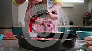 Home cooking. A woman in an apron grates cheese on top of a pizza. Hands close up