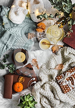 Home coziness still life - soft slippers, knitted sweater, plaid, green tea with honey, tangerines, dry leaves, books, garland,