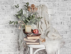 Home cozy still life - an old vintage chair, stack of books, knitted plaid, candle, apple fruit. Hobby, leisure, comfort concept.