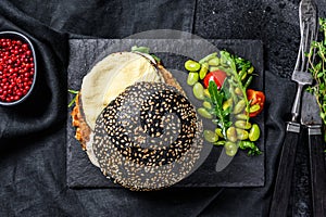 Home craft Burger with a black bun, scrambled eggs, and arugula. Blackburger. Black background. Top view