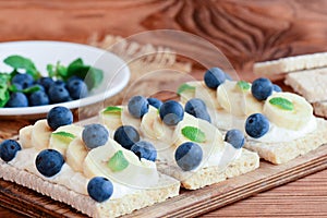 Home crispbread toast with cottage cheese, banana and berries on wooden board. Healthy sandwiches with cottage cheese photo