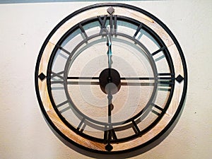 Home decoration concept. Wall clock that is made of black steel Which has 4 Roman numbers. It is hung on a light brown wall.