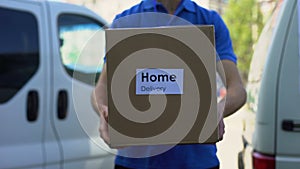 Home delivery service courier in uniform holding cardboard box, express shipping