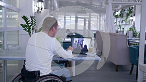 Home education, senior crippled man in wheel chair writes notes in notebook while watching online training on laptop