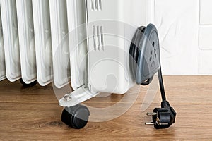 Home electric oil heater on plastic twin wheels and with cable reeled up on a cable storage. White oil-filled radiator on a brown