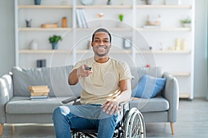 Home entertainments. Happy disabled African American guy with TV controller enjoying movie indoors