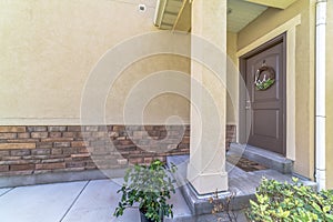 Home entrance with doorstep small porch and brown wooden front door with wreath