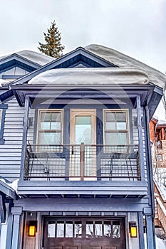 Home exterior with snowy gable roof over balcony and glass paned garage door.