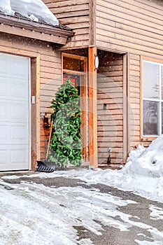 Home facade with snowy driveway and simple Christmas tree by the door in winter