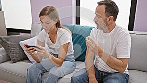 At home, father and daughter in a heated argument over smartphone usage, sitting unhappily on the sofa in their living room,