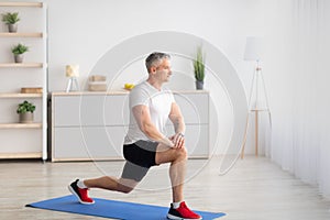 Home fitness. Motivated mature man doing lunges in living room interior, free space, banner design photo