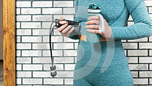 Home fitness workout concept. Cordless jump rope and water bottle in hands of a women in sportswear. Modern sports accessories for