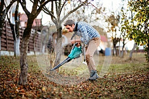 Home gardening details, man cleaning up the garden using leaf blower photo