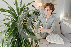 Home gardening. Happy senior woman with glasses caring for the plant. Smiling elderly woman spraying aloe vera with a