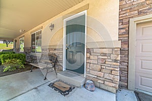 Home with green door yard windows and porch bench against stone brick wall