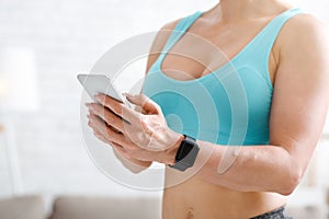 Home gym. Woman with smart watch and phone in hand in light interior