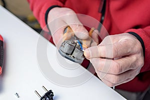 Home hobby. Close-up of a Caucasian man holding a wire insulation tool, a stripper working on an electrical cord on a white