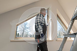 Home improvement concept, handyman painting a wall with a white paint near roof window in attic