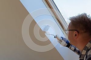 Home improvement concept, handyman painting a wall with a white paint near roof window in attic