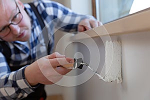 Home improvement concept, handyman painting a wall with a white paint near roof window in attic