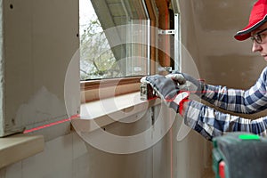 Home improvement handyman installing window sill in new build attic by using leveler and laser leveler