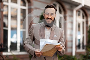 Home inheritance. Happy male heir with documents in hands on the background of real estate. Buying a house, won the court photo