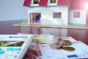 Home insurance concept with blurred background focused on bills, coins and calculator, house concept on background