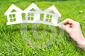 Home insurance concept with hand holding house shaped printouts on green grass