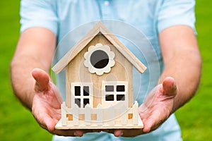 Home insurance concept. Real estate agent holding house model on grass background. Sell house, finance and mortgage