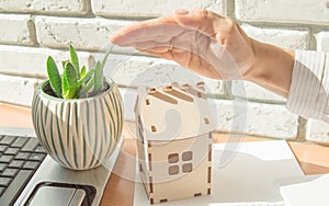 Home insurance concept, a woman holds her protective hand over a small wooden house