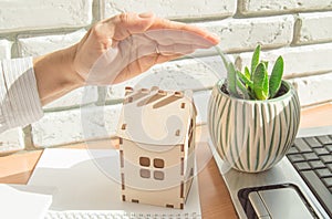 Home insurance concept, a woman holds her protective hand over a small wooden house