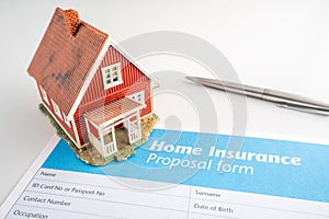 Home insurance proposal form with miniature red house and pen laying on white office desk.