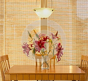 Home interior kitchen dining room with wood table and chairs, lighting fixture, fresh flowers and natural window coverings blinds