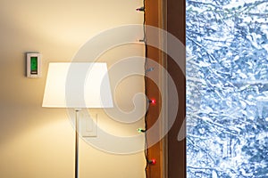 Home interior living room in winter with digital electronic thermostat, floor lamp and view through windows of snowy outdoors