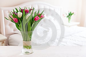 Home interior with pink tulips in a vase on a light bedroom background